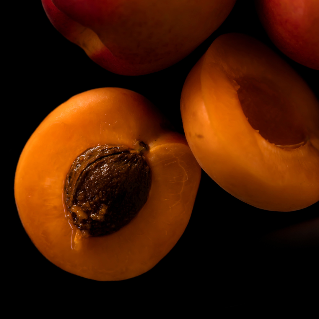 Close-up of ripe apricots with one halved to reveal the kernel inside, set against a dark background to highlight the fruit’s vibrant orange color.