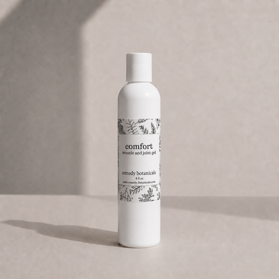 A white bottle of Comfort Muscle and Joint Gel by Simply Botanicals, standing on a neutral beige surface with soft shadows.