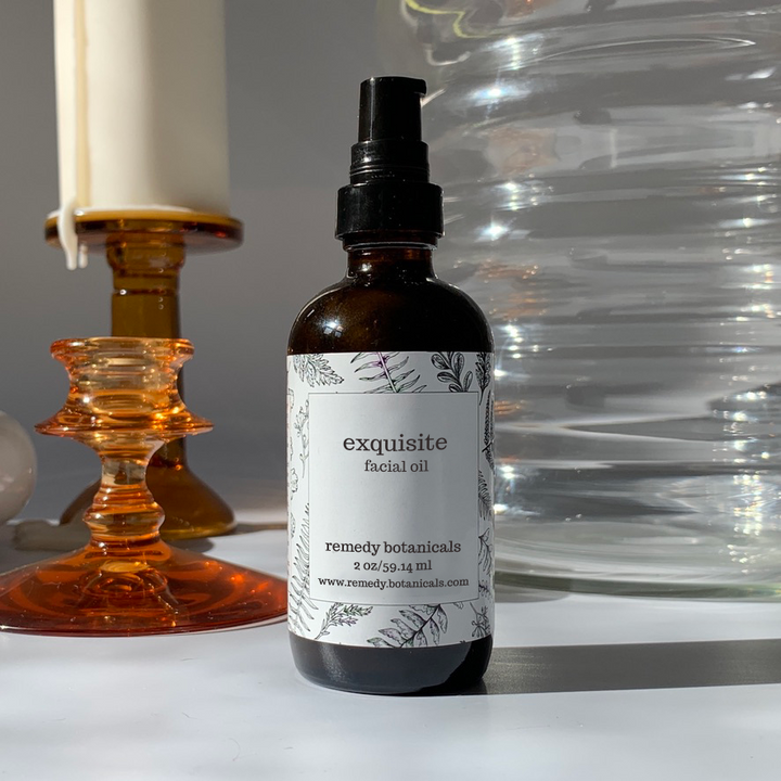 Exquisite Facial Oil amber pump bottle on a tabletop with amber candleholders, a clear glass vase.