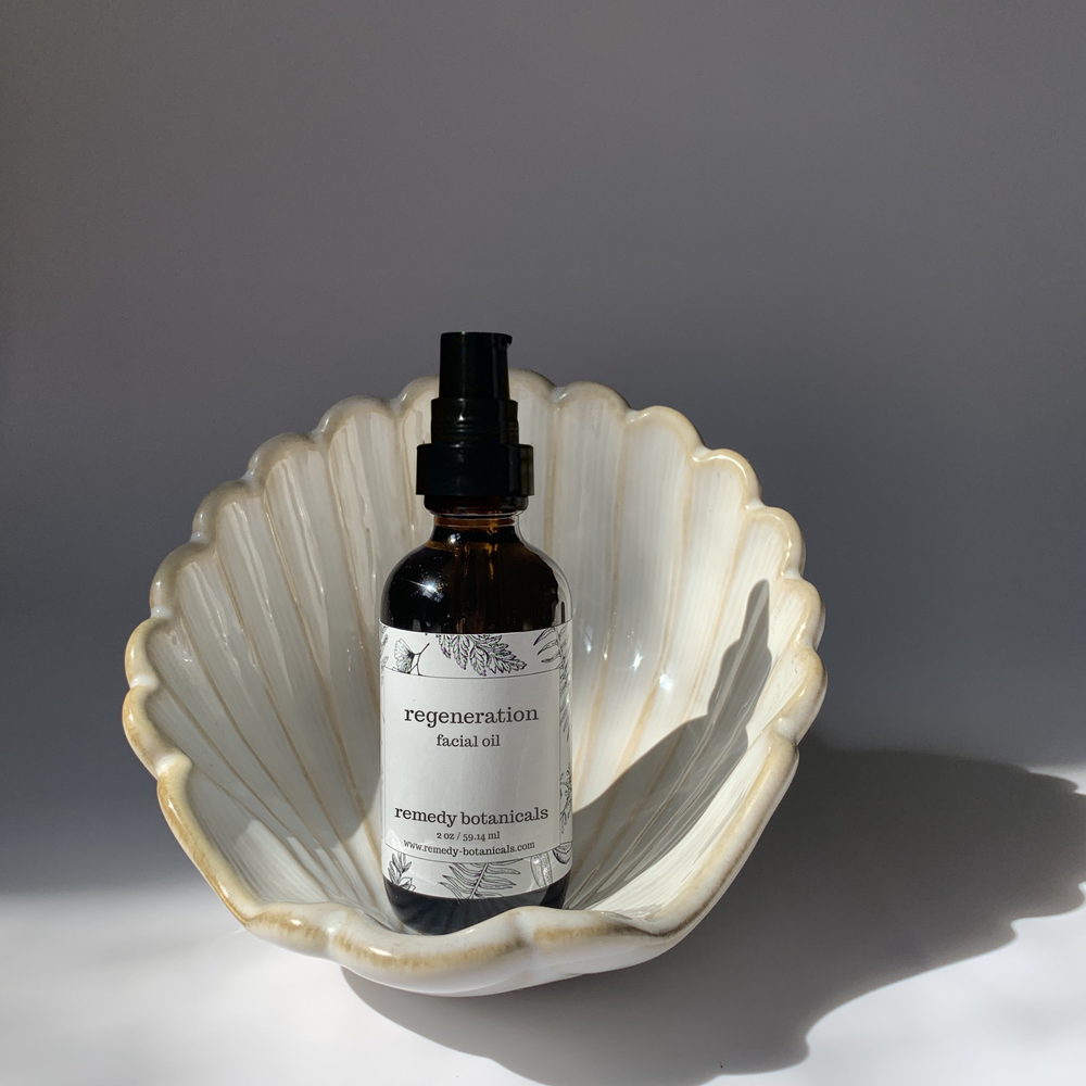 Facial oil bottle labeled 'regeneration' in a shell-shaped dish on a gray background