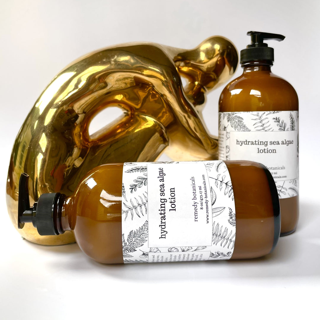 Two amber pump bottles of Remedy Botanicals lotion displayed beside a sculptural golden mask.
