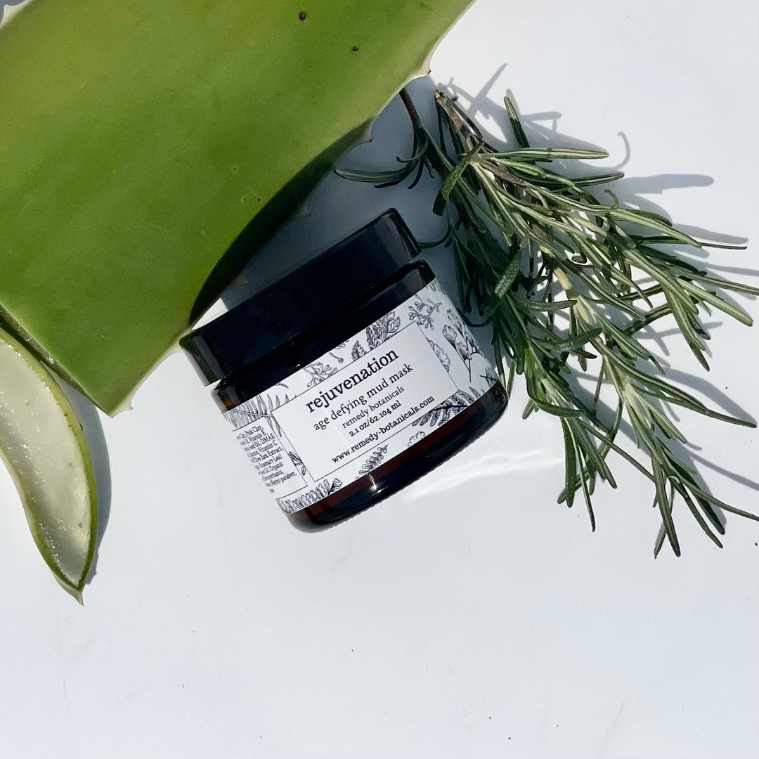 Amber jar placed on its side with aloe vera leaf and rosemary sprigs on a white background.