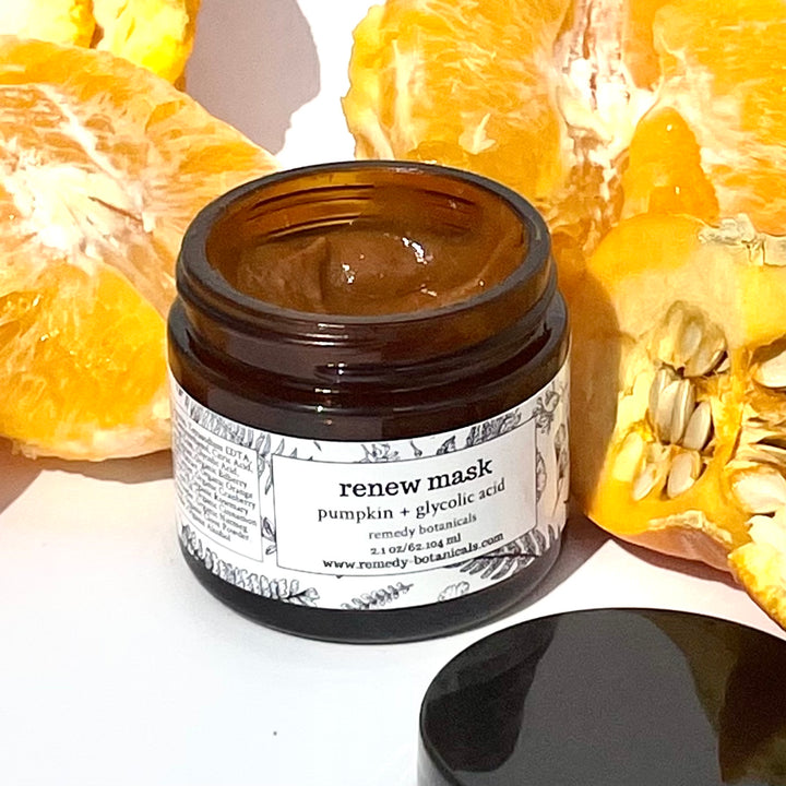 Amber jar with black lid, displayed among fresh orange slices and peels on a white surface.